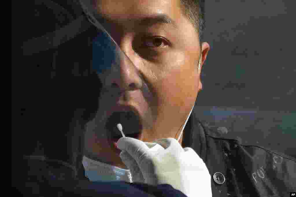 A man gets his routine COVID-19 throat swab at a coronavirus testing site in Beijing. Access to an industrial zone in the central Chinese city of Zhengzhou was suspended after the city reported 64 coronavirus cases and workers who assemble Apple Inc. iPhones left their factory in the zone following outbreaks.