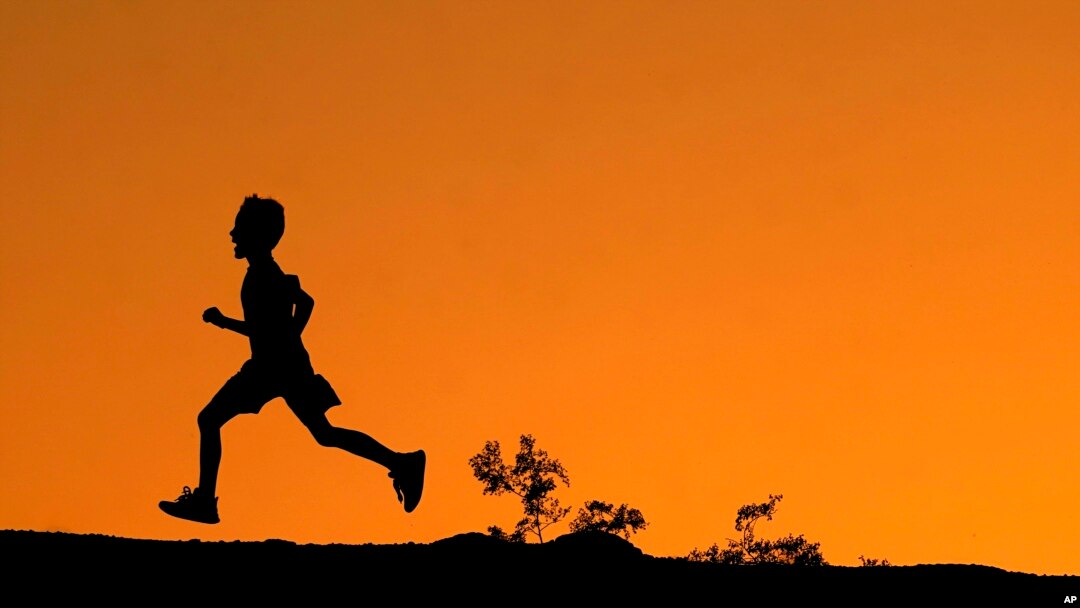 La silueta de un niño se recorta contra el cielo al atardecer mientras corre a lo largo de una cresta en Papago Park, el viernes 1 de abril de 2022, en Phoenix. (Foto AP/Charlie Riedel)