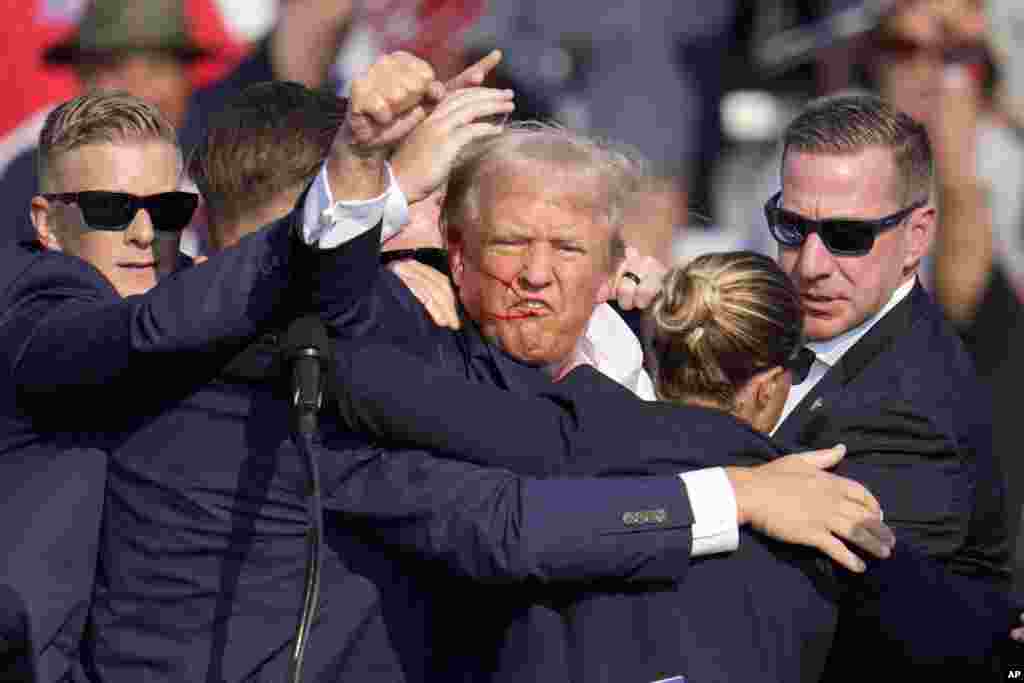 Republican presidential candidate former President Donald Trump pumps his fist as he is helped off the stage at a campaign event in Butler, Pensylvania, July 13, 2024. Trump was wounded during an assassination attempt while speaking at the rally.