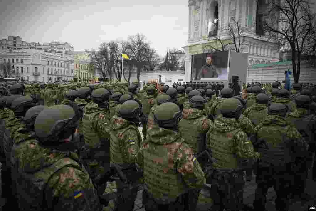 Ukrainian servicemen and servicewomen attend a ceremony with Ukrainian President Volodymyr Zelenskyy shown on a screen at St Sophia Square in Kyiv. (Photo taken and released by Ukrainian Presidential press service)