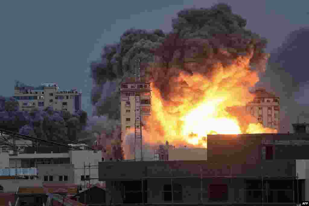 People standing on a rooftop watch as a ball of fire and smoke rises above a building in Gaza City, Oct. 7, 2023 during an Israeli airstrike that hit the Palestine Tower building. 