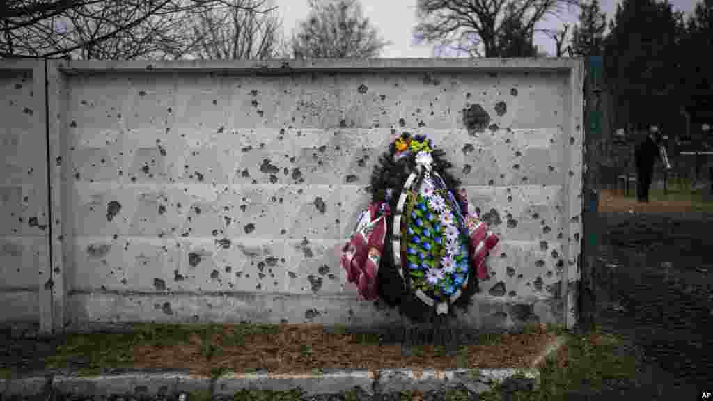 A wreath leans against a shrapnel-damaged wall in the cemetery where a funeral for an officer of the 93rd Ukrainian brigade was being held in Bucha, near Kyiv, Ukraine.