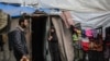 A Palestinian man walks past as a woman stands at the entrance of a tent in an area housing displaced people in Rafah, in the southern Gaza Strip, on April 30, 2024.