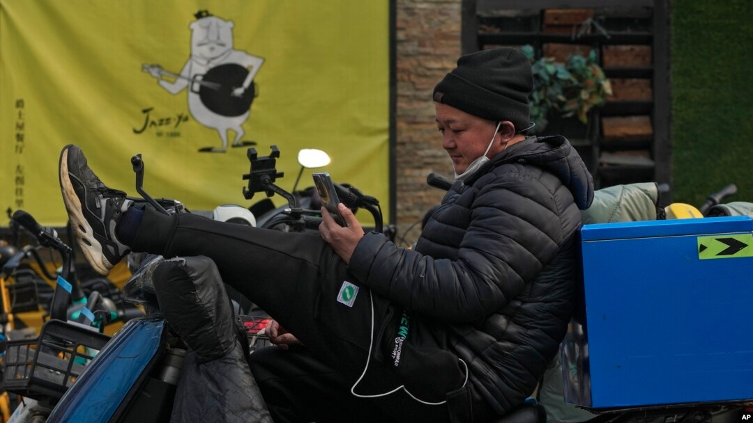 FILE - A man sits on his bike watching video from a social media app via his smartphone on a street in Beijing, Feb. 27, 2023. 