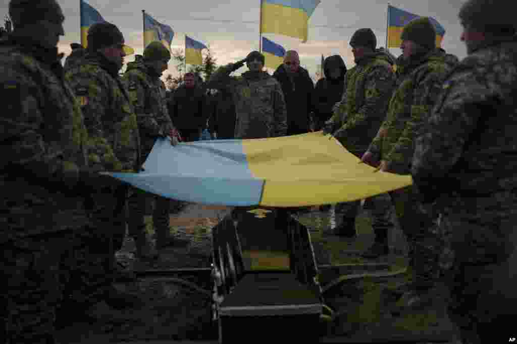 Ukrainian soldiers hold their national flag over the coffin of a comrade during his funeral in Bucha, on the outskirts of Kyiv, Ukraine.