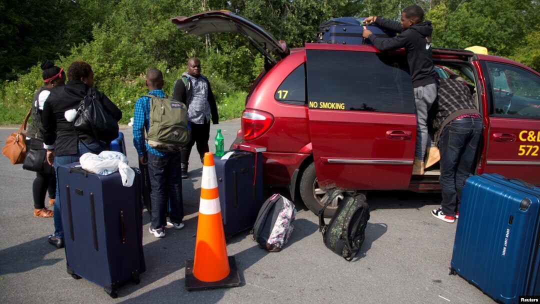 FILE - A refugee family claiming to be from Haiti take their luggage from their taxi as they arrive at the U.S.-Canada border on Roxham Road in Champlain, New York, August 3, 2017.