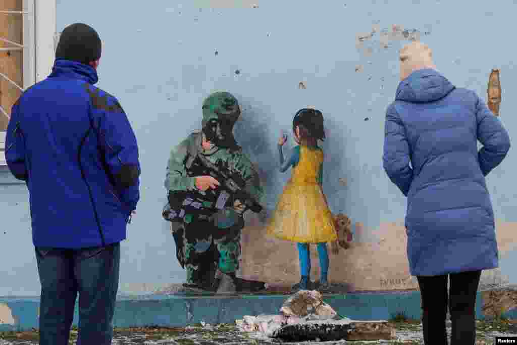 People look at an artwork of the famous street artist Tvboy, created on a wall of the House of Culture, which was heavily damaged during Russia's attack on Ukraine, in the town of Irpin, outside Kyiv.
