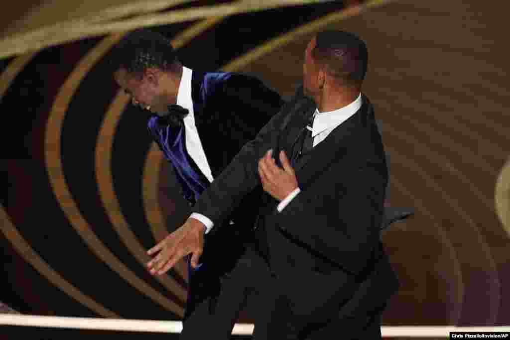 American actor Will Smith, right, hits presenter Chris Rock on stage while presenting the award for best documentary feature at the Oscars, March 27, 2022, at the Dolby Theatre in Los Angeles, California.