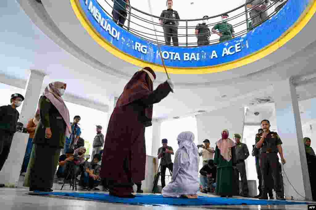 A woman is caned by a Sharia policeman as a punishment for being caught in close proximity with a man in Banda Aceh, Indonesia.