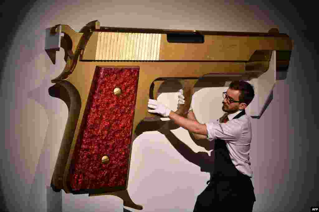 An employee poses with an enlarged model gun entitled "James Bond's New Gun," designed by David Collins and Floris Van Den Broecke for Granda Publishing LTD., 1977, at Sotheby's auction house in London.