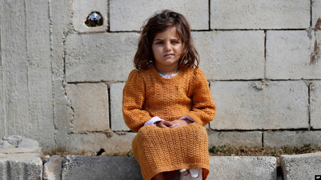 FILE - A displaced Syrian girl sits outside her family's tent at a refugee camp in Bar Elias, Bekaa Valley, Lebanon, March 5, 2021. 