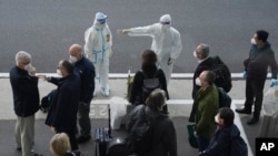 調查新冠病毒源頭的世衛專家們抵達武漢天河國際機場，身穿防護服的中國工作人員給他們指方向。（2021年1月14日-美聯社）