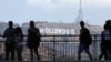 FILE - Tourists walk past the Hollywood sign as they visit a shopping complex along Hollywood Boulevard in Hollywood, California, Aug. 3, 2017.