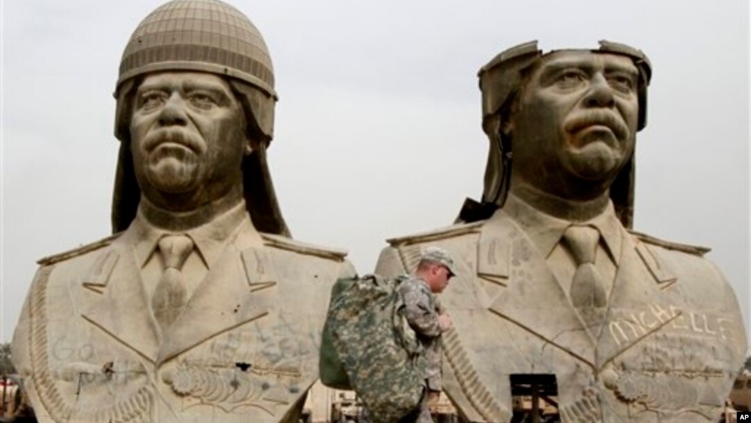 FILE - U.S. soldiers walk past two gigantic status of former Iraqi President Saddam Hussein in Baghdad, March 20, 2009.