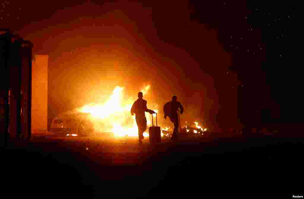People run while a vehicle is burning during riots at Hal Far Open Centre migrant camp in Hal Far, Malta, Oct. 21, 2019.