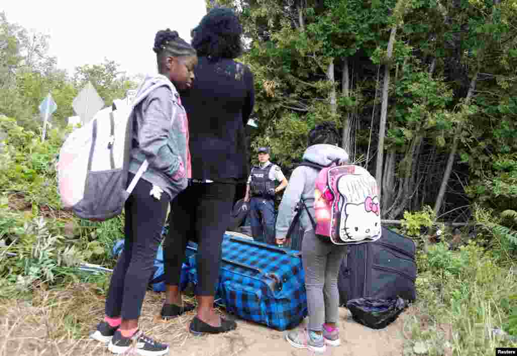 A family who identified themselves as from Haiti are confronted by a Royal Canadian Mounted Police officer as they try to enter into Canada from Roxham Road in Champlain, New York, Aug. 7, 2017.