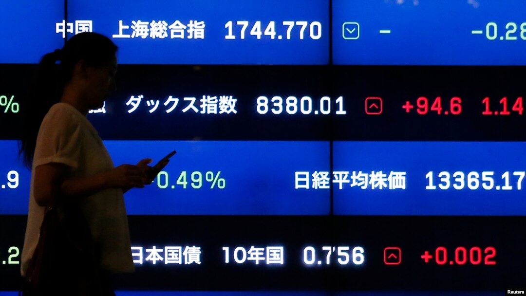 FILE - A woman walks past a screen showing market indices in Tokyo. The International Monetary Fund says that for advanced economies, debt has risen to more than 107 percent of their national economic output, while Japan is almost at 250 percent.