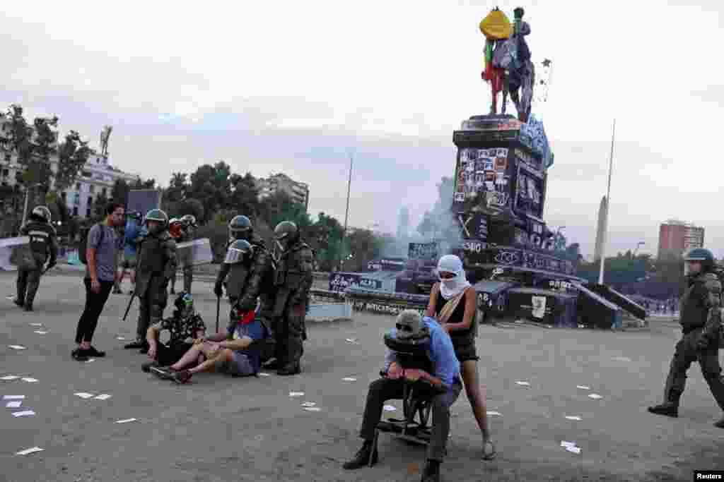 A man receives a massage from a demonstrator while riot policemen confront others during an anti-government protest at Plaza Italia in Santiago, Chile, Dec. 2, 2019.