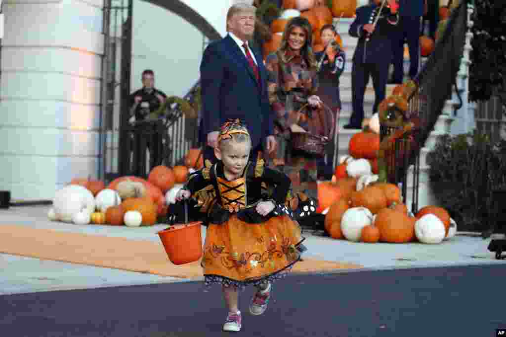 President Donald Trump and first lady Melania Trump watch a young girl as they give candy to children during a Halloween trick-or-treat event on the South Lawn of the White House, Oct. 28, 2019, in Washington.