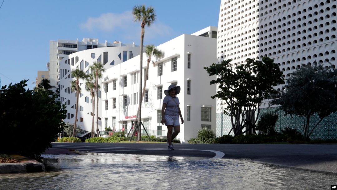 FILE - A woman walks along a flooded street caused by a kind of tide called a king tide on September 28, 2019, in Miami Beach, Florida. (AP Photo/Lynne Sladky, File)