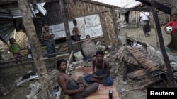 FILE - Rohingya people pass their time in a damaged shelter in Rohingya IDP camp outside Sittwe, Rakhine state, Aug. 4, 2015. 