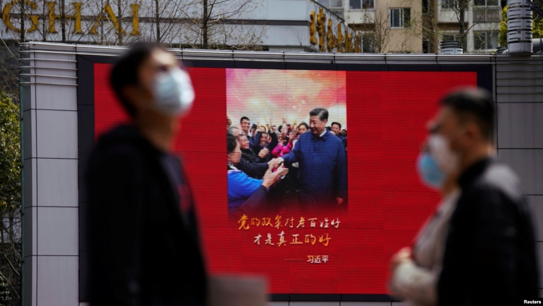 Pedestrians wearing face masks walk past a screen displaying an image of Chinese President Xi Jinping after the city's emergency alert level for coronavirus disease (COVID-19) was downgraded, in Shanghai, China March 23, 2020. REUTERS/Aly Song