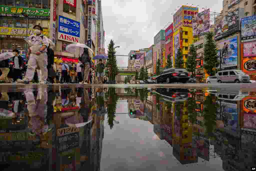 People wearing protective masks are reflected in a puddle as they walk across a street in a shopping district in Tokyo. Japan fully came out of a coronavirus state of emergency for the first time in more than six months on October 1.