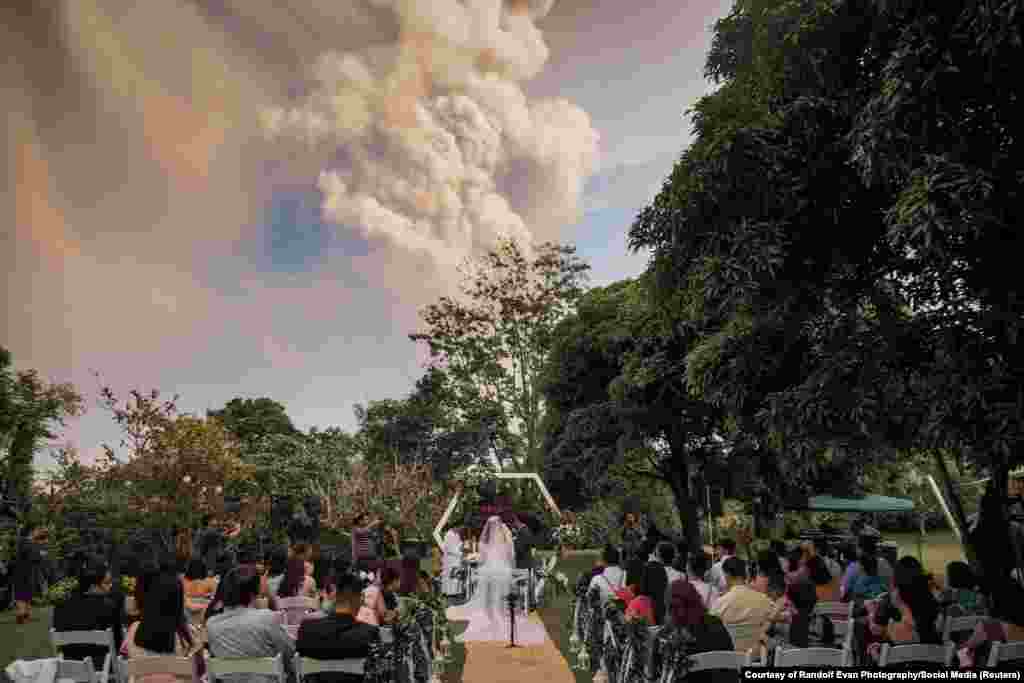 People attend a wedding ceremony as Taal Volcano sends out a column of ash in the background in Alfonso, Cavite, Philippines, in this image obtained from social media.