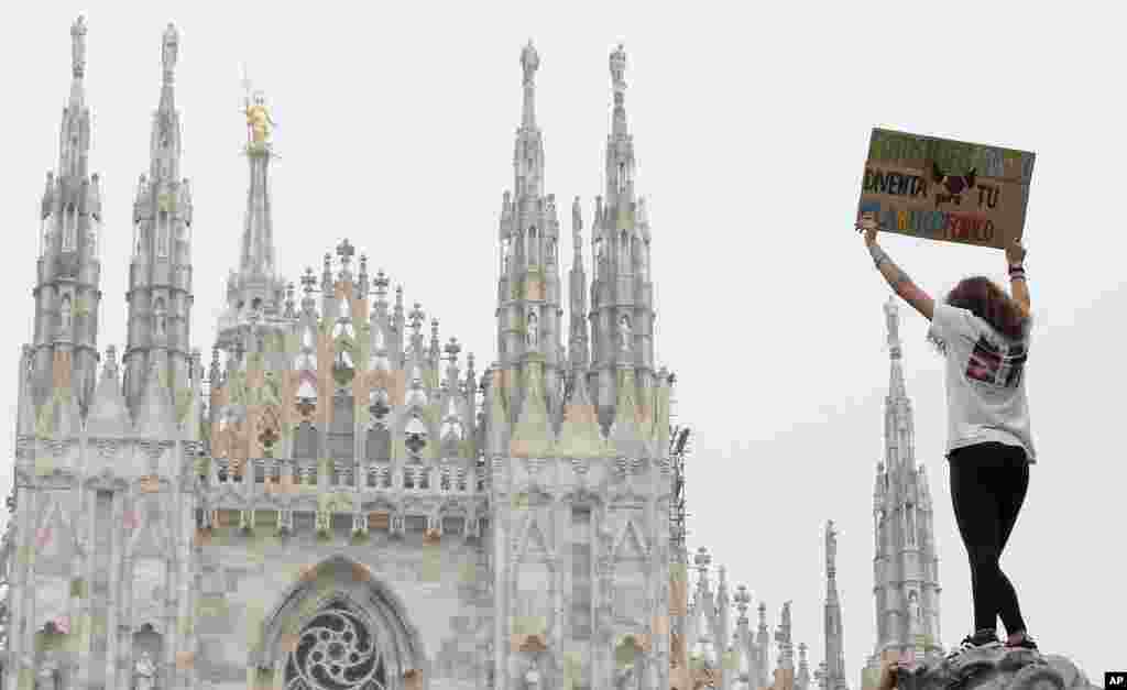 A girl holds up a card with writing reading in Italian "Lets photosynthesize, also you become plastic phobic" during a worldwide protest demanding action on climate change in front of Milan's gothic cathedral, Italy.