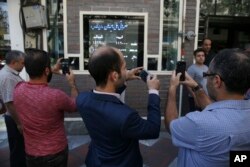 FILE - Iranians take pictures of an exchange shop screen showing various currency rates in downtown Tehran, Oct. 2, 2018. Iran's currency, the rial, had unexpectedly rallied after weeks of depreciation following President Donald Trump's decision to withdraw America from Tehran's nuclear deal with world powers, sending Iranians rushing to exchange shops to cash in.
