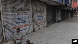 Một người bàn hàng rong ở Karachi ngồi cạnh dãy cửa hàng đóng cửa vì tình trạng bạo động trong thành phố
