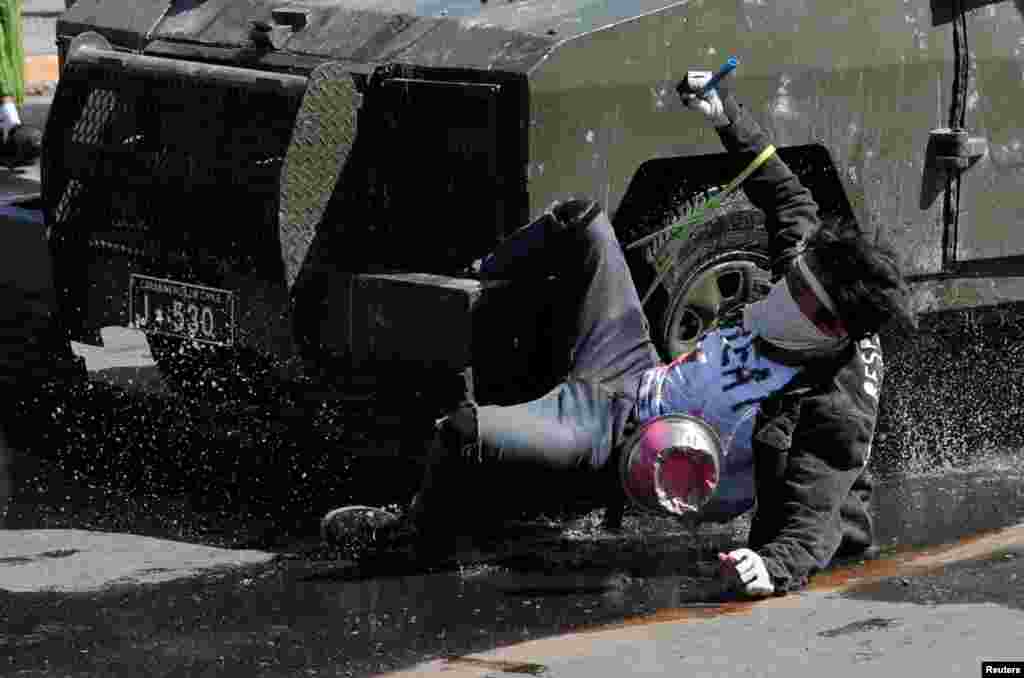 A demonstrator hangs from a riot police vehicle during a protest against Chile's state economic model in Santiago, Oct. 20, 2019.