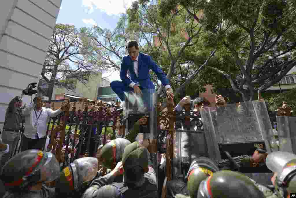 Venezuela’s National Assembly President and opposition leader Juan Guaido tries to climb the fence to enter the compound of the Assembly in Caracas, after he and other opposition lawmakers were blocked by police from entering a session to elect new Assembly, Jan. 5, 2020.