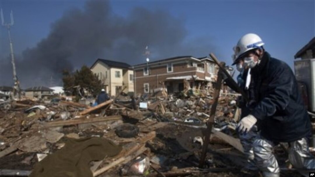 A body, covered in a blanket, lies in the rubble of a destroyed neighborhood as firefighters search the area in Sendai, Miyagi Prefecture, northeastern Japan, two days after a giant quake and tsunami struck the country's northeastern coast, March 13, 2011