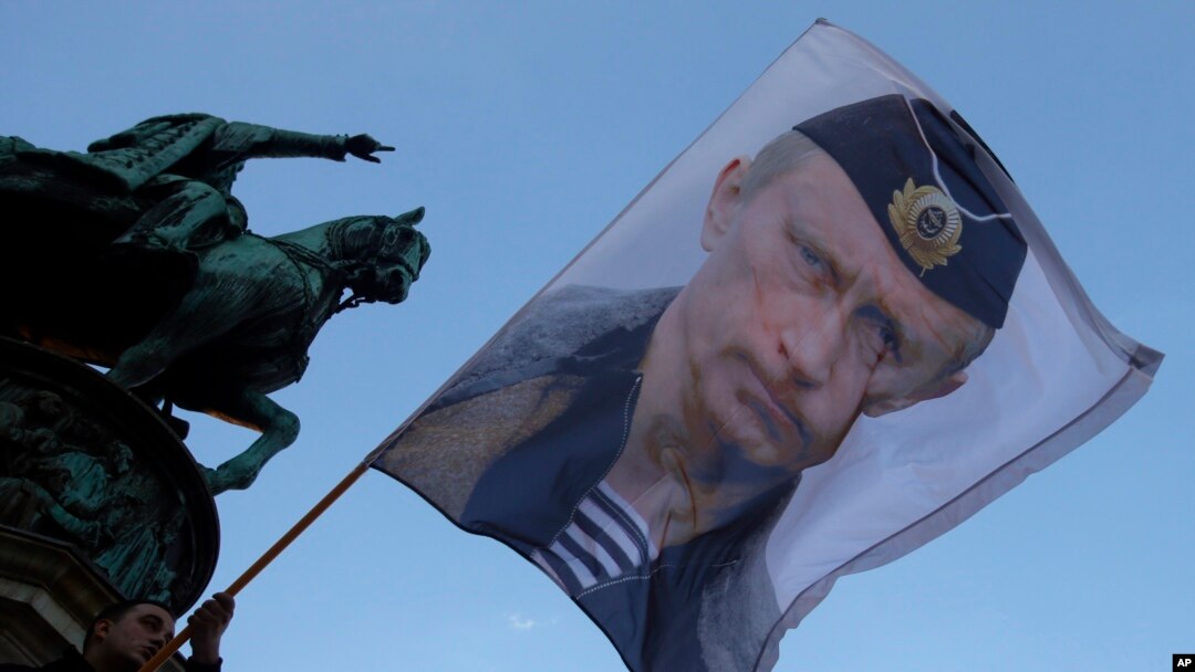 FILE - A man waves a flag showing Russian President Vladimir Putin in front of the monument of late Serbian Duke Mihailo Obrenovic in Belgrade, Serbia, Sept. 24, 2016.