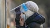 A woman wearing a face mask and face shield get ready for her routine COVID-19 throat swab at a coronavirus testing site in Beijing, Dec. 7, 2022. 