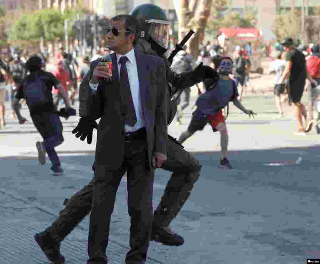A man drinks a Frucola as a policeman chases demonstrators during a protest against Chile's government in Santiago, Dec. 4, 2019.