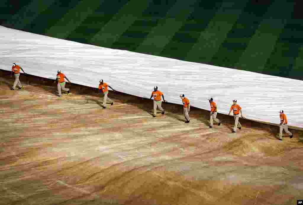 Groundskeepers remove a tarp from the field during a rain delay between the first and second baseball games of a doubleheader between the Baltimore Orioles and the Pittsburgh Pirates, May 1, 2014, in Maryland.
