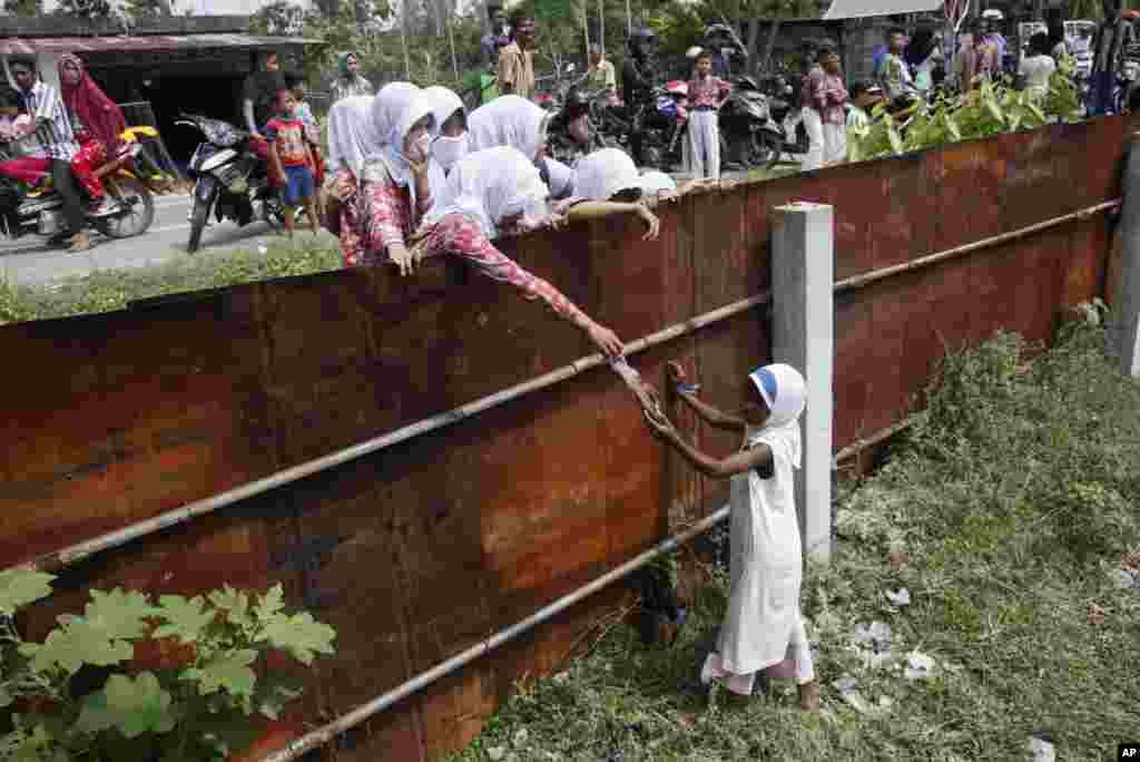 Các học sinh Indonesia đưa thực phẩm cho một bé gái Rohingya từ bên ngoài hàng rào của nơi trú ẩn tạm thời cho di dân ở Bayeun, tỉnh Aceh, Indonesia, ngày 21/5/2015.