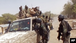 In this photo taken on Thursday, Feb. 19, 2015, Chadian soldiers on top of a truck, left, speak to Cameroon soldiers, right, standing next to the truck, on the border between Cameroon and Nigeria as they form part of the force to combat regional Islamic extremists force's including Boko Haram, near the town of Fotokol, Cameroon. 