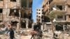 People stand in front of damaged buildings, in the town of Douma, the site of a chemical weapons attack, near Damascus, on April 16, 2018. (Hassan Ammar/AP) 