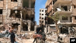 People stand in front of damaged buildings, in the town of Douma, the site of a chemical weapons attack, near Damascus, on April 16, 2018. (Hassan Ammar/AP) 