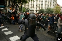 FILE - A member of the Spanish riot police swings a club against would-be voters near a school assigned to be a polling station by the Catalan government in Barcelona, Spain, Oct. 1, 2017.