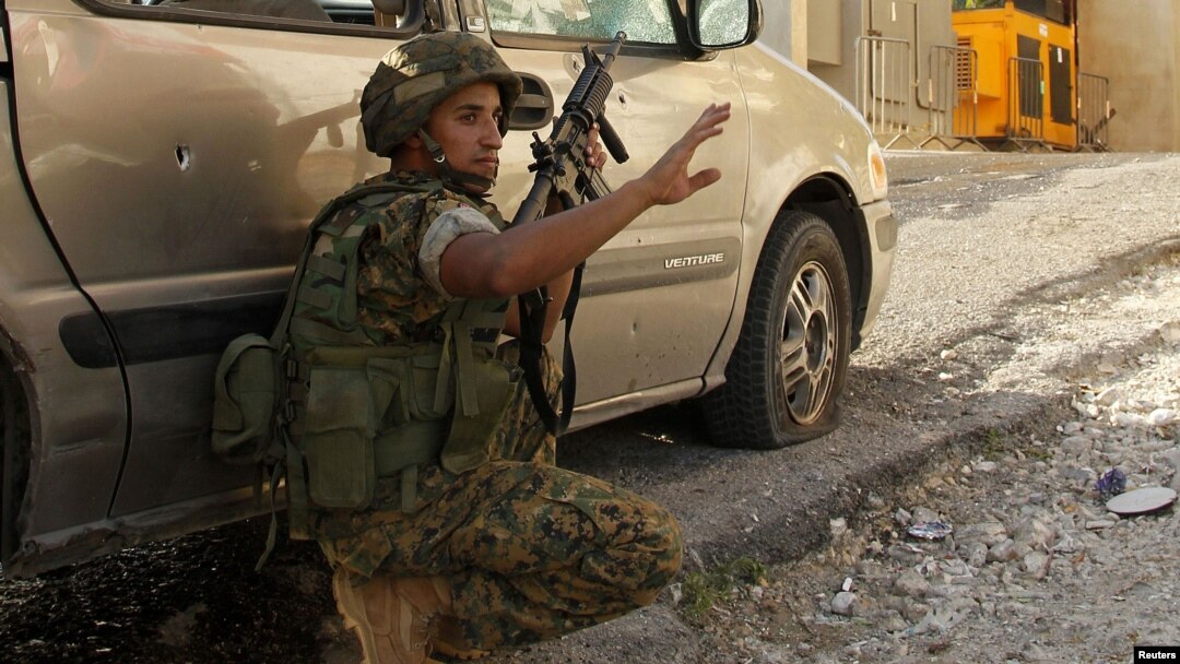 A Lebanese army soldier takes a position behind a car near the mosque complex (background), where hardline Sunni cleric Sheikh Ahmed al-Assir was believed to be sheltering with his supporters in Abra near Sidon, southern Lebanon, June 24, 2013.