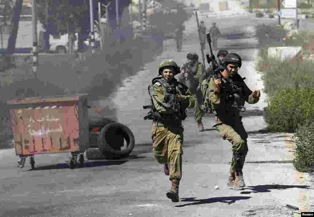 Israeli soldiers run during clashes with Palestinian protesters at a demonstration against the Israeli offensive in Gaza, near the Israeli settlement of Bet El, near Ramallah, July 25, 2014. 