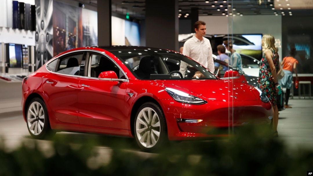 FILE- In this July 6, 2018, file photo, a prospective customer confer with sales associate as a Model 3 sits on display in a Tesla showroom in the Cherry Creek Mall in Denver.