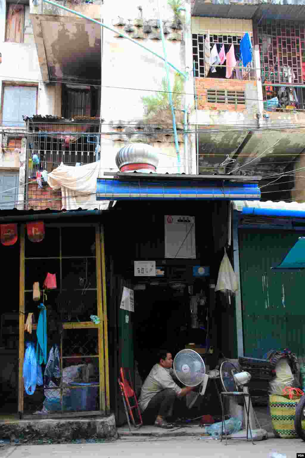 A mechanic fixes fans in his small electrical shop on the ground floor of the White Building, Phnom Penh, Cambodia, Sept. 5, 2014. (Nov Povleakhena/VOA)