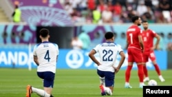 Dos jugadores de la selección inglesa de fútbol, Declan Rice y Jude Bellingham, se arrodillan el 21 de noviembre de 2021, en el estadio Khalifa de Doha, antes de comenzar su primer partido de la Copa del Mundo de Qatar 2022, frente a Irán, país que en las últimas semanas se ha vuelto foco de las críticas por su violenta represión de las recientes protestas.