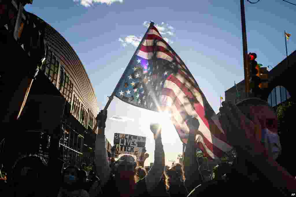 A man holds a U.S. flag upside down, a sign of distress, as protesters march down the street during a solidarity rally for George Floyd, May 31, 2020, in the Brooklyn borough of New York.