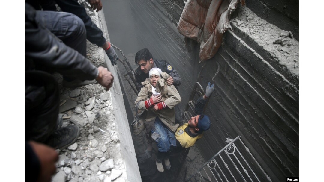 Syria civil defense workers help an unconscious woman from a shelter in the besieged town of Douma, eastern Ghouta, Damascus, Syria, Feb. 22, 2018.